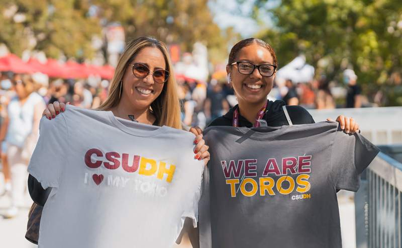 Two people holding CSUDH shirts.