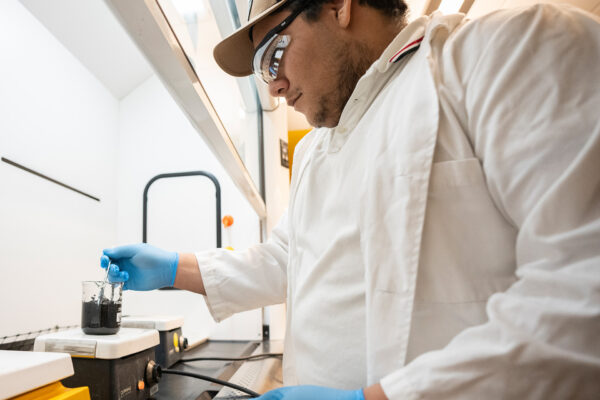 Person in lab coat dips instrument into beaker of biochar.