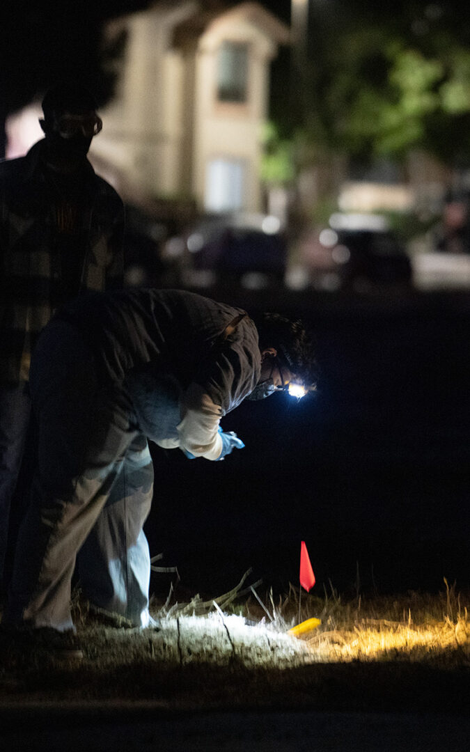 Student bent over to inspect crime scene marker on ground.