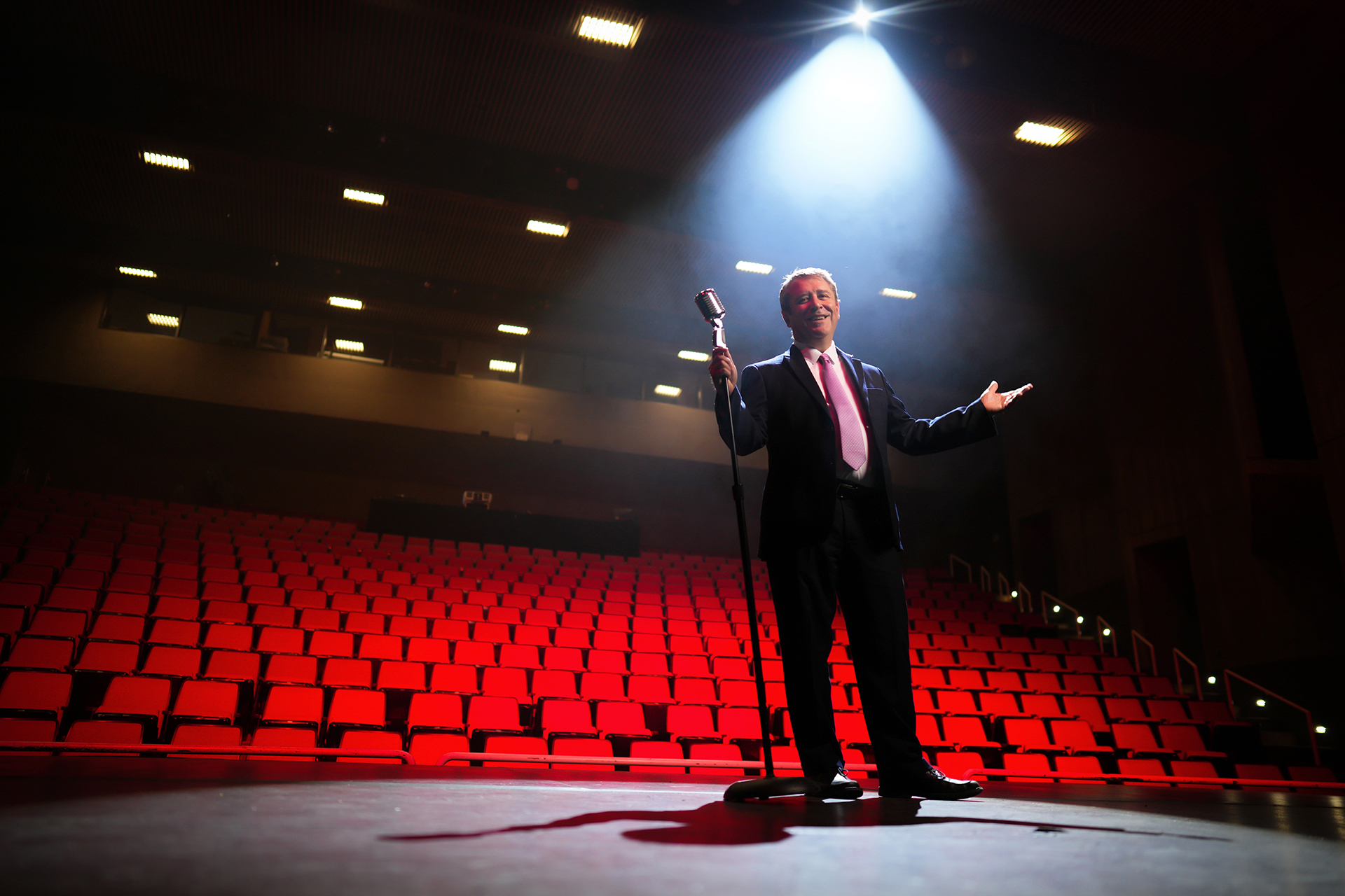 Dean Caron on stage in the University Theater, with rows of seats on view in background.