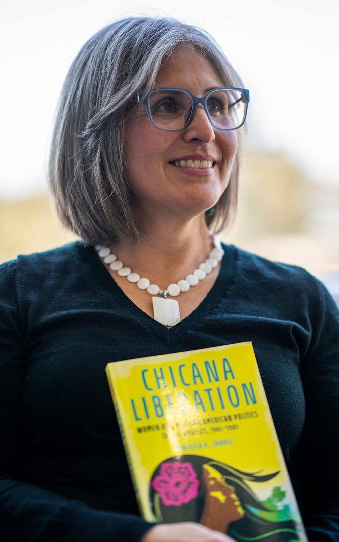 Marisela wearing classes and a chunky white necklace. She's holding her book.