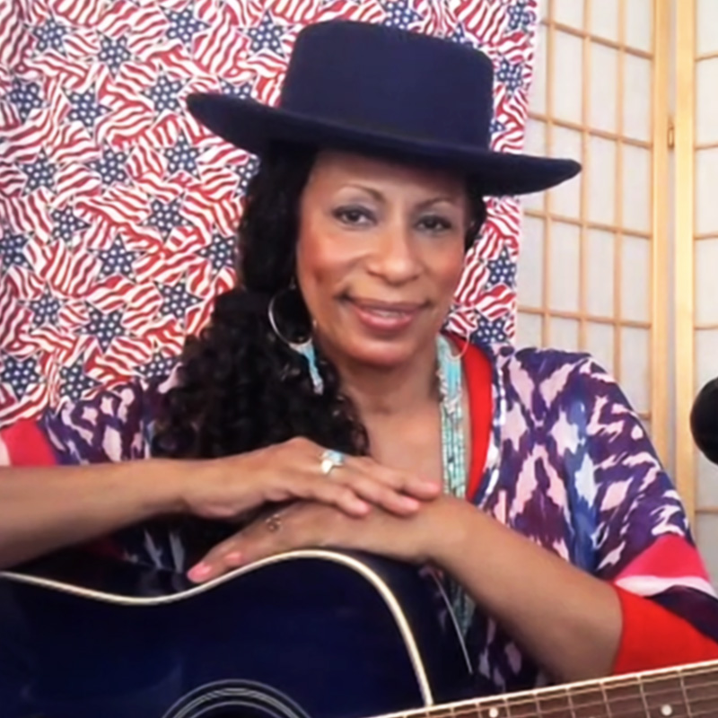 Person posing with guitar, wearing a black hat.